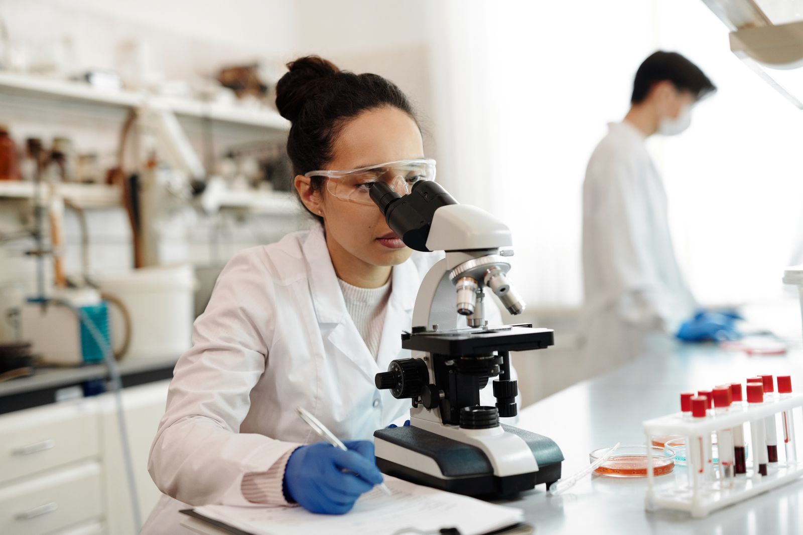 Wetenschapper in laboratoriumjas kijkt door een microscoop in een modern lab